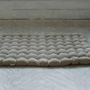 May include: A beige linen floor cushion with a tufted design. The cushion is made of multiple small, round, button-like tufts.