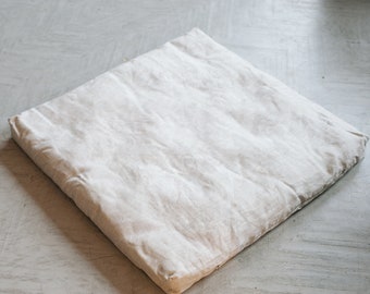 Puede incluir: Un cojín blanco liso de forma cuadrada y tejido suave y texturizado.
