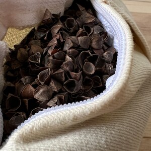 May include: A white fabric bag with a zipper closure filled with buckwheat hulls. The bag is lying on a wooden surface.