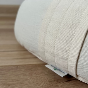 May include: Close-up of a white, organic cotton cushion with a label that reads "Hemp & Organic Cotton". The cushion is made of thick, natural fabric and has a simple, minimalist design.