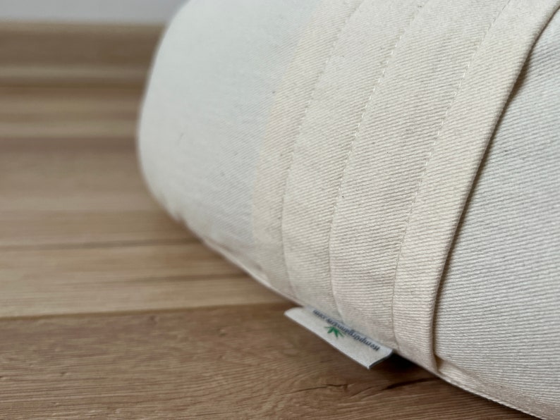 May include: Close-up of a white, organic cotton cushion with a label that reads "Hemp & Organic Cotton". The cushion is made of thick, natural fabric and has a simple, minimalist design.