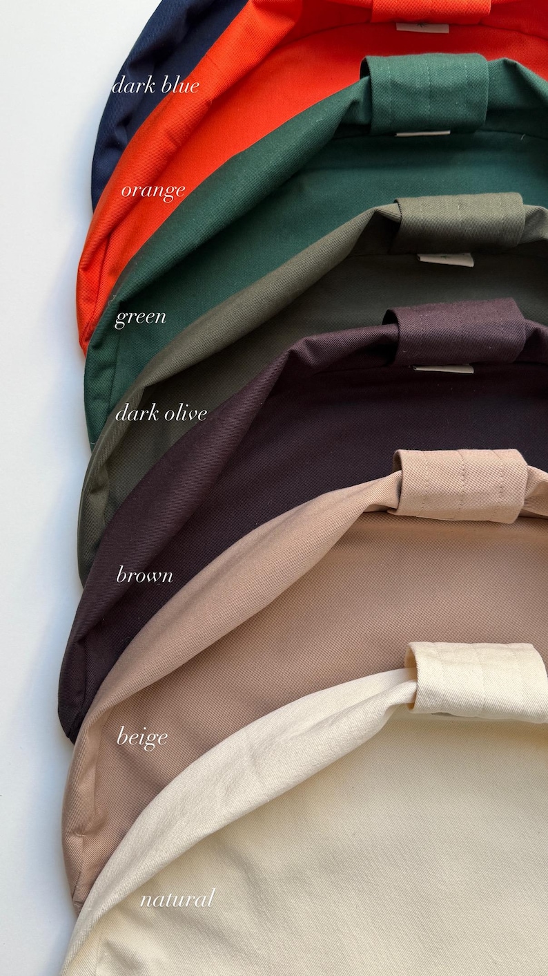 May include: A collection of fabric bags stacked vertically, featuring a range of colors labeled as dark blue, orange, green, dark olive, brown, beige, and natural. Each bag has a visible top handle strap and a smooth, solid-colored textile finish.