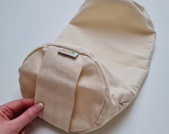 May include: Cream-colored rectangular yoga bolster with a rounded end. The bolster has a sewn-in handle and a small tag that reads "HEMP". The bolster is made of a natural, unbleached fabric.