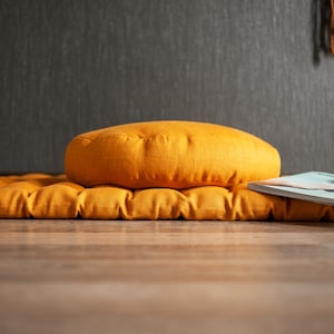 May include: A yellow meditation cushion with a matching yellow cushion on top. A magazine is placed on top of the cushions.