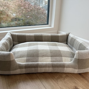 Puede incluir: Una cama rectangular para perros con un estampado de cuadros beige y blanco. La cama tiene laterales elevados para mayor comodidad. La cama está hecha de una tela suave y duradera y está diseñada para mascotas. Aproximadamente 70 cm de largo.