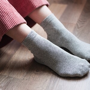 May include: A pair of gray ankle socks on a wooden floor. The socks are made of a soft, comfortable material.