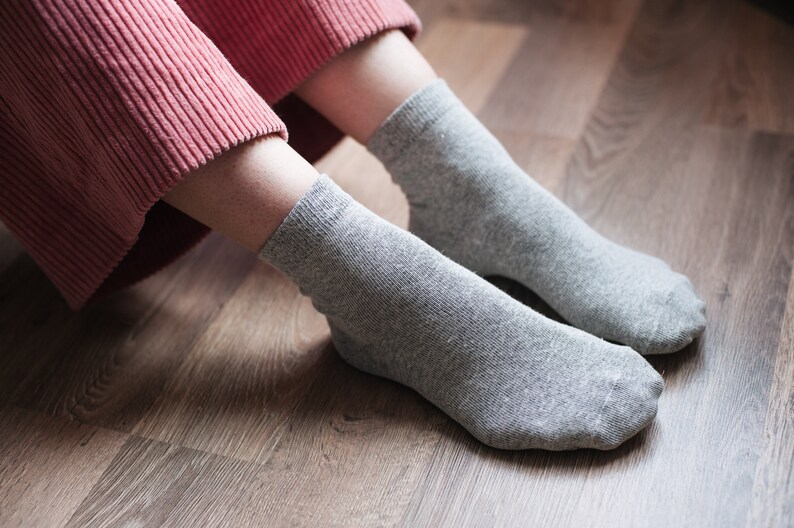 May include: A pair of gray ankle socks on a wooden floor. The socks are made of a soft, comfortable material.