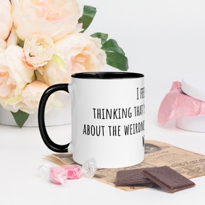 May include: White coffee mug with a black handle and black rim. The mug has black text that reads "I feel like thinking that about the weirdness of the world".