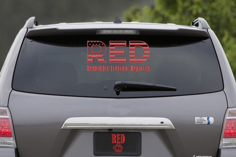 May include: A gray SUV with a red and white American flag sticker on the back window. The sticker says "RED" with the letters made of the American flag and the words "Remember Everyone Deployed" below. The car also has a license plate that says "RED" with a small American flag design.