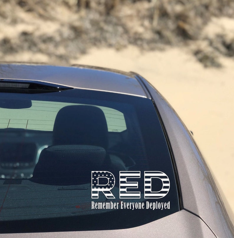 May include: A white vinyl car sticker with the acronym "RED" in large letters, with each letter designed to look like the American flag. Below the letters is the text "Remember Everyone Deployed".