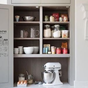 May include: A white kitchen cabinet with glass shelves filled with various food items and kitchen tools. The cabinet door has a black and white kitchen conversion chart sticker with the text "Kitchen Conversions".