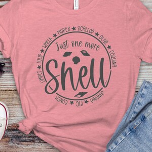 May include: A pink t-shirt with a gray circle design that says "Just one more shell" with the names of different types of shells around the circle.