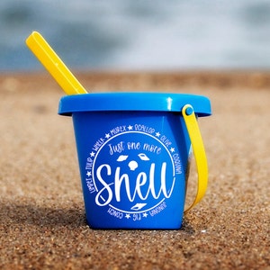May include: A blue plastic beach pail with a yellow handle and a white graphic that says "Just one more shell" surrounded by the names of different types of shells.