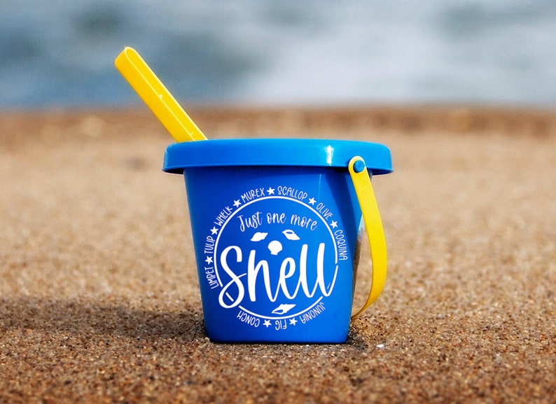 May include: A blue plastic beach pail with a yellow handle and a white graphic that says "Just one more shell" surrounded by the names of different types of shells.