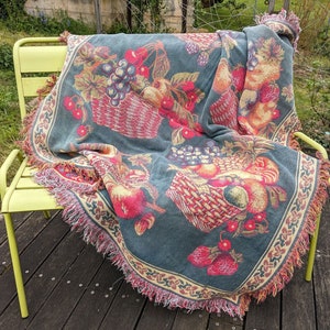 Peut inclure: Une couverture en jeté de couleur sarcelle avec un motif de panier de fruits. La couverture présente des images de pommes, de raisins, de fraises et de cerises. La couverture a une bordure décorative et des franges.