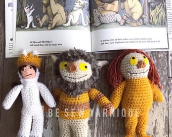 May include: Three crocheted stuffed toys inspired by the characters from the book "Where the Wild Things Are". The toys are a white furry creature with a crown, a brown and yellow striped creature with fur, and a yellow creature with long orange hair.