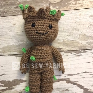 May include: A crocheted plush toy of Groot from Guardians of the Galaxy. The toy is brown with green leaves and has a smiling face.