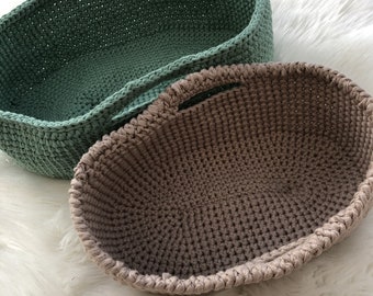 May include: Two crocheted baskets, one green and one brown, with handles. The baskets are oval shaped and made of a soft, textured yarn.