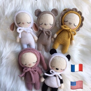 Puede incluir: Cinco patrones de animales de peluche tejidos a crochet, cada uno con un diseño de animal diferente: un cordero, un oso, un león, un conejito y un panda. Los animales llevan todos atuendos con capucha y tienen los ojos cerrados. El texto "Les Capu' Choux" y "Toujours Un Fil à la Patte" es visible en la imagen. La imagen también incluye las banderas de Francia y los Estados Unidos. El texto "5 patrons" también es visible en la imagen.