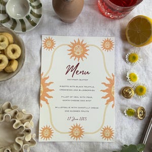 Op de afbeelding: Een menukaart met een zonontwerp, met het woord "Menu" in bordeauxrood schrift. Het menu bevat antipasti-buffetitems, waaronder risotto, kalfsvlees en millefoglie. De datum "27 juni 2025" staat ook op de kaart.