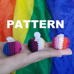 Puede incluir: Se muestran tres pequeños objetos de ganchillo coloridos con detalles blancos y ojos negros. Los objetos son en tonos de azul, rosa, morado, blanco, naranja y amarillo. La palabra "PATTERN" se muestra en letras blancas.