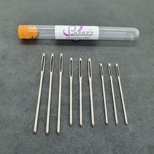 May include: A set of eight silver needles in a clear plastic tube with a bright orange cap. The tube has the text "Pazazz" and "www.pazazz.wales" printed on it.
