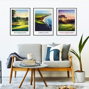 May include: Three framed landscape prints featuring golf courses. The prints are labeled "Bethpage Black", "Cabot Cliffs", and "Royal Melbourne". The prints are displayed above a gray sofa with decorative pillows and a small wooden table.