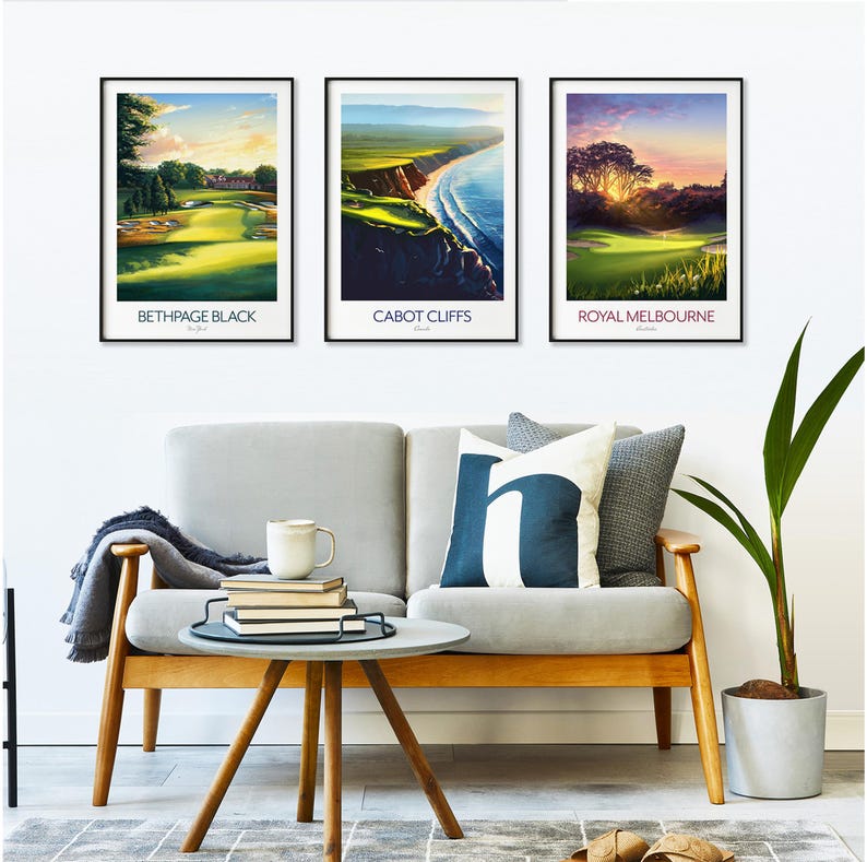May include: Three framed landscape prints featuring golf courses. The prints are labeled "Bethpage Black", "Cabot Cliffs", and "Royal Melbourne". The prints are displayed above a gray sofa with decorative pillows and a small wooden table.