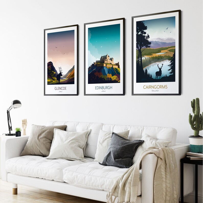 May include: Three framed prints of Scottish landscapes. The first print shows a silhouette of a deer in a mountainous landscape with a lake. The second print shows a castle on a hill with a blue sky and white clouds. The third print shows a mountain range with a lake in the foreground. The prints are all in a minimalist style with bold colors and simple lines.