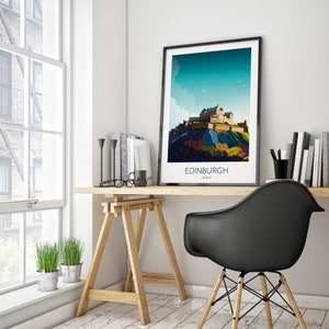 May include: A black framed print of a colorful illustration of Edinburgh Castle in Scotland. The print is hanging on a white wall above a wooden desk with a black chair and a potted plant.