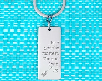 Puede incluir: Llavero de plata con una etiqueta rectangular que dice "I love you the mostest. The end. I win." con una flecha y un símbolo de corazón y la letra K.
