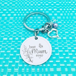 May include: Silver keychain with a round charm that says "best Mum ever" with a butterfly and leaves design. The keychain also has a small silver heart charm and a purple bead.