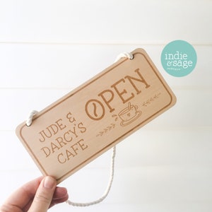 May include: A wooden sign with a rope hanger that reads "Jude & Darcy's Cafe" and "Open" with a coffee cup graphic.