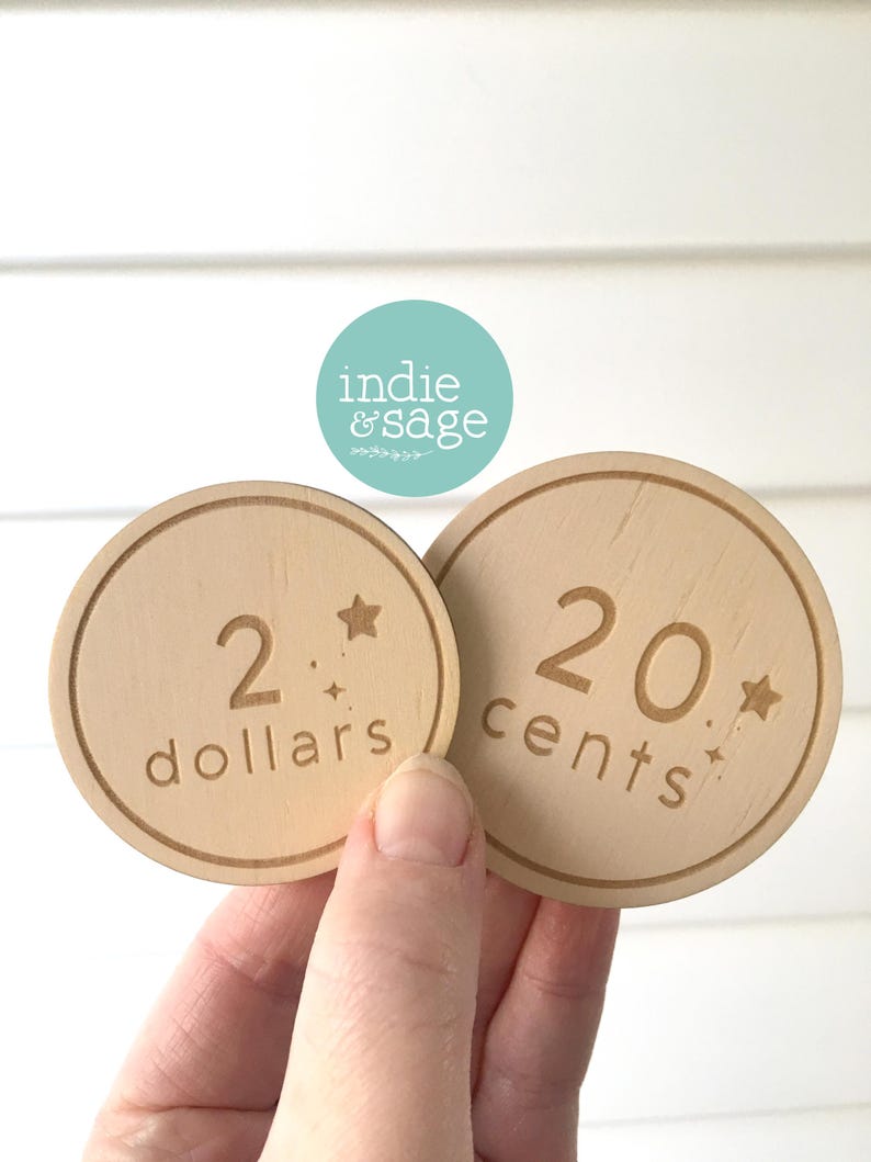 May include: Two wooden play money coins. One coin reads "2 dollars" and the other reads "20 cents". Both coins have a star and small starburst design. The brand logo "indie & sage" is visible in the background.