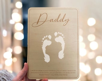 May include: A wooden plaque with the word "Daddy" engraved in cursive script. The plaque features two white footprints and a message that reads "I want to follow in your footsteps, you are what I want to be. because in all the world, you are the best role model for me. Happy Father's day 2023, Love Darcy."