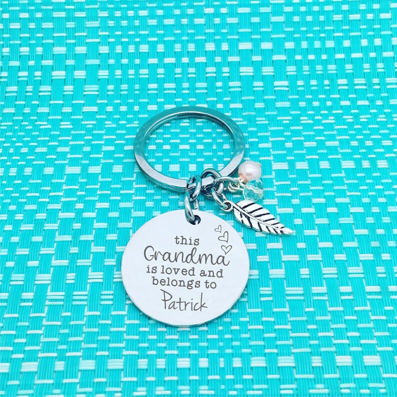 May include: Silver keyring with a round charm that says "this Grandma is loved and belongs to Patrick" with two small hearts and a silver feather charm.