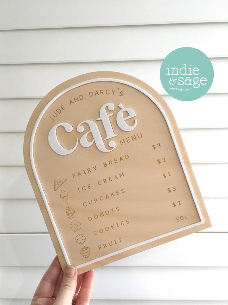 May include: A wooden cafe menu with a light brown surface and a white border. The menu lists items like fairy bread, ice cream, and donuts. The cafe's name, "Jude and Darcy's Cafe," is displayed at the top.
