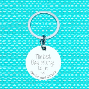 Puede incluir: Llavero de plata con una etiqueta redonda que dice "El mejor pap&aacute; nos pertenece Jayden y Callum" con un s&iacute;mbolo de coraz&oacute;n.