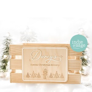 May include: A wooden crate with a light-coloured wooden sign that reads "Darcy's Special Christmas delivery". The sign has a white border and features a Christmas tree and nutcracker design. The crate is made of light-coloured wood.