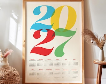 May include: A framed wall calendar for the year 2027 featuring large, overlapping stylized numbers in blue, yellow, red, and green. Below the numbers, the calendar displays the months from January to December with small black text for dates.