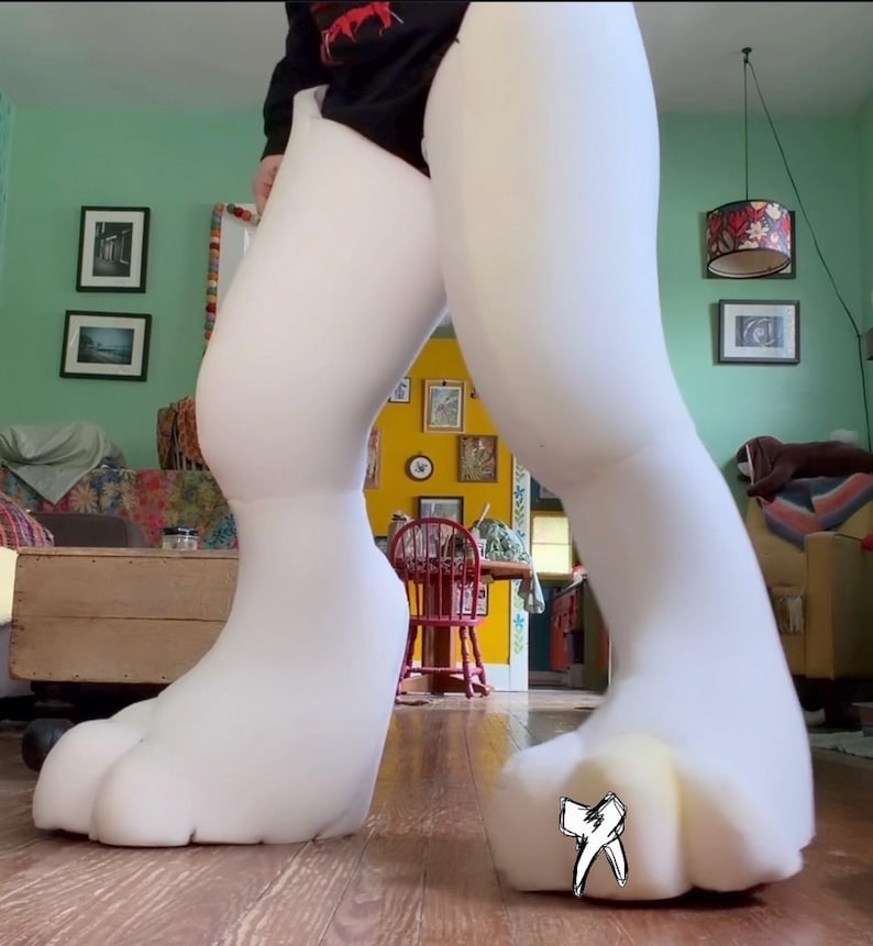 May include: A pair of oversized, white foam leg and foot coverings designed for a costume. The feet feature large, rounded toes, and a small black and white line drawing of a tooth is visible on the top of the right foot. The foam is smooth.