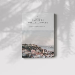Peut inclure: Une couverture de livre avec le titre "Carnet de Voyage a Broder" et le sous-titre "Inspirations Lisboetes". La couverture présente une photographie d'une ville avec des bâtiments sur une colline surplombant une étendue d'eau.