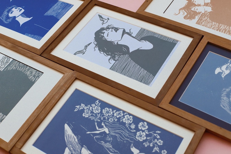 May include: A collection of framed art prints with wooden frames. The prints feature illustrations in shades of blue, gray, and tan. The artwork depicts figures, flowers, and abstract designs. The frames are arranged at various angles, creating a visually appealing display.