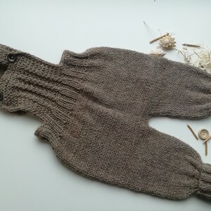 Puede incluir: Un par de petos de bebé de punto color topo. Los petos tienen tirantes con cierres de botón y puños acanalados en los tobillos. La prenda está hecha de un hilo suave y texturizado.