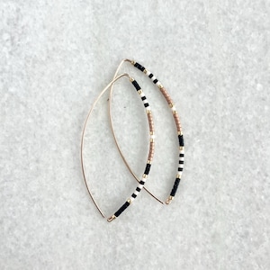 May include: A pair of gold hoop earrings featuring black, white and brown beads. The beads are arranged in a geometric design.