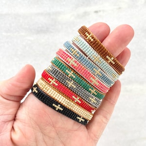 Puede incluir: Una pila de pulseras de cuentas de colores con detalles dorados. Las pulseras están hechas con cuentas pequeñas y tienen un patrón de cruz.