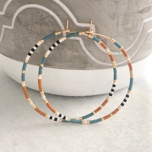 May include: A pair of large hoop earrings with a multi-colored beaded design. The beads are in shades of orange, white, black, and teal.
