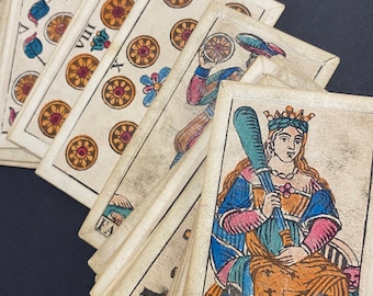 May include: A set of vintage playing cards with colorful illustrations. The cards are arranged in a fan shape, revealing a queen holding a club and wearing a crown. The cards have a worn, antique look.