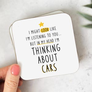 May include: White coaster with black text that reads "I might look like I'm listening to you... but in my head I'm thinking about cars". A yellow star is above the text.