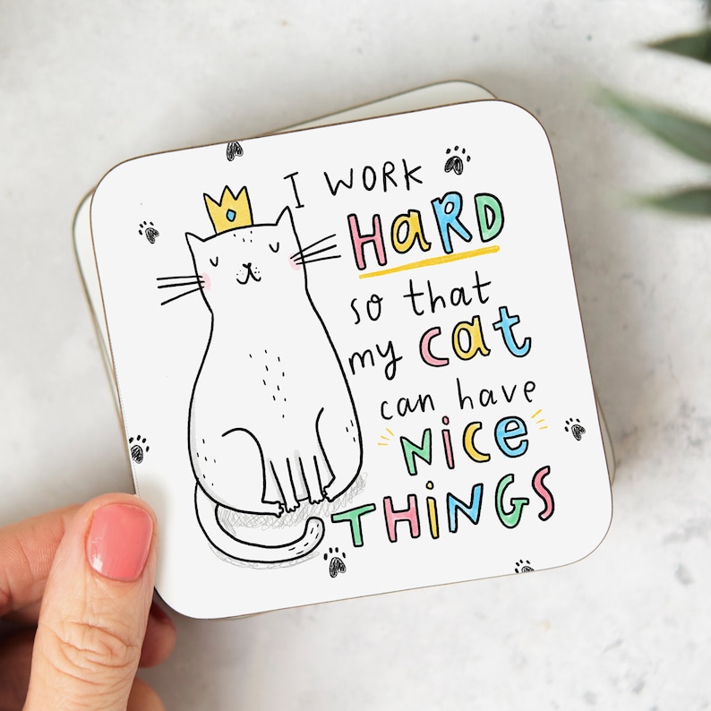 May include: White coaster with a cartoon cat wearing a gold crown. The text reads "I work hard so that my cat can have nice things".